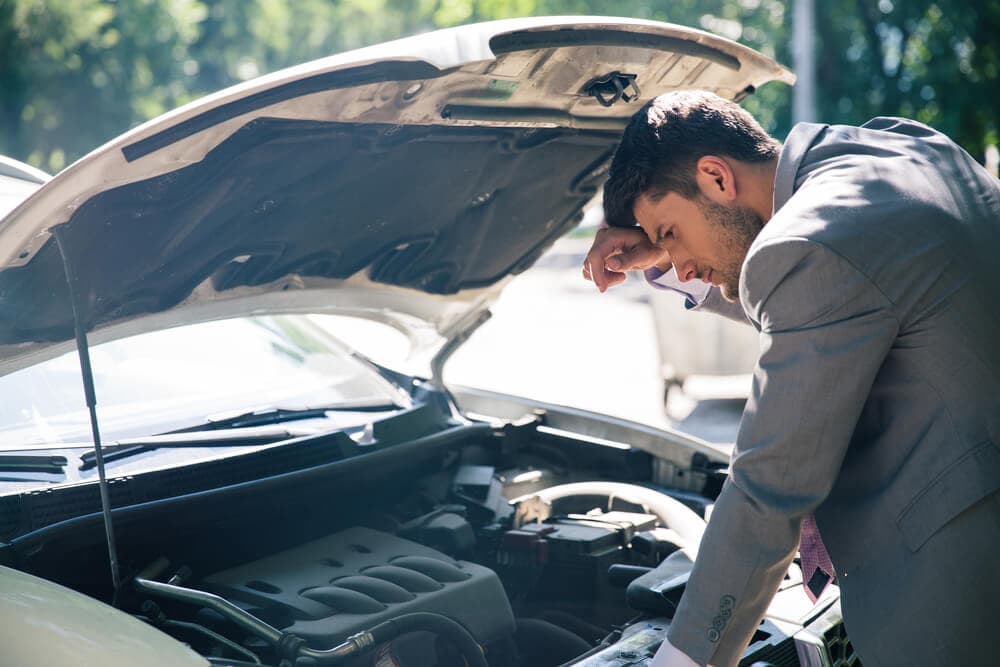 worried man looking at broken down car engine