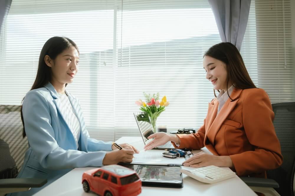 Two professionals review auto policy paperwork across a desk with a toy car and calculator, highlighting independent agent strategies to boost car insurance renewals.