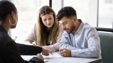 Independent agent reviewing policy documents with a couple at a desk, highlighting independent agent strategies to boost car insurance renewals.