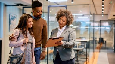 Happy,Insurance,Agent,And,African,American,Couple,Analyzing,Documents,On Insurance agent reviewing coverage options on a clipboard with a couple in a modern office during an insurance consultation.