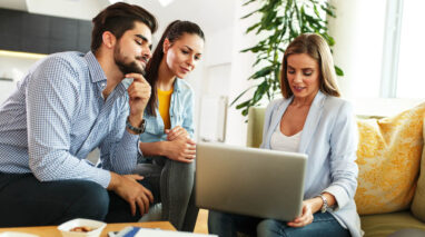 A female insurance agent works on a laptop with a couple buying insurance.