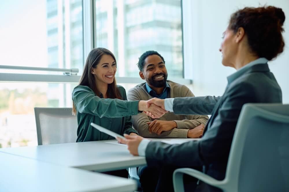 Woman insurance agent shakes hands with woman in biracial couple customers.