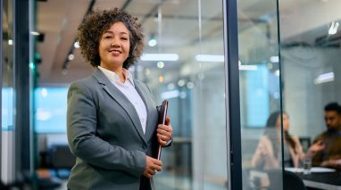 BF-future-of-independent-insurance-agents-1 An independent insurance agent stands confidently in a modern office holding a tablet, ready to guide clients through personalized insurance decisions.