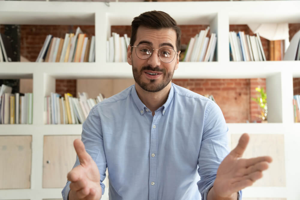 Smiling young insurance agent sits at desk talking on webcam using social media to generate leads for his insurance agency, and partnering with the best.