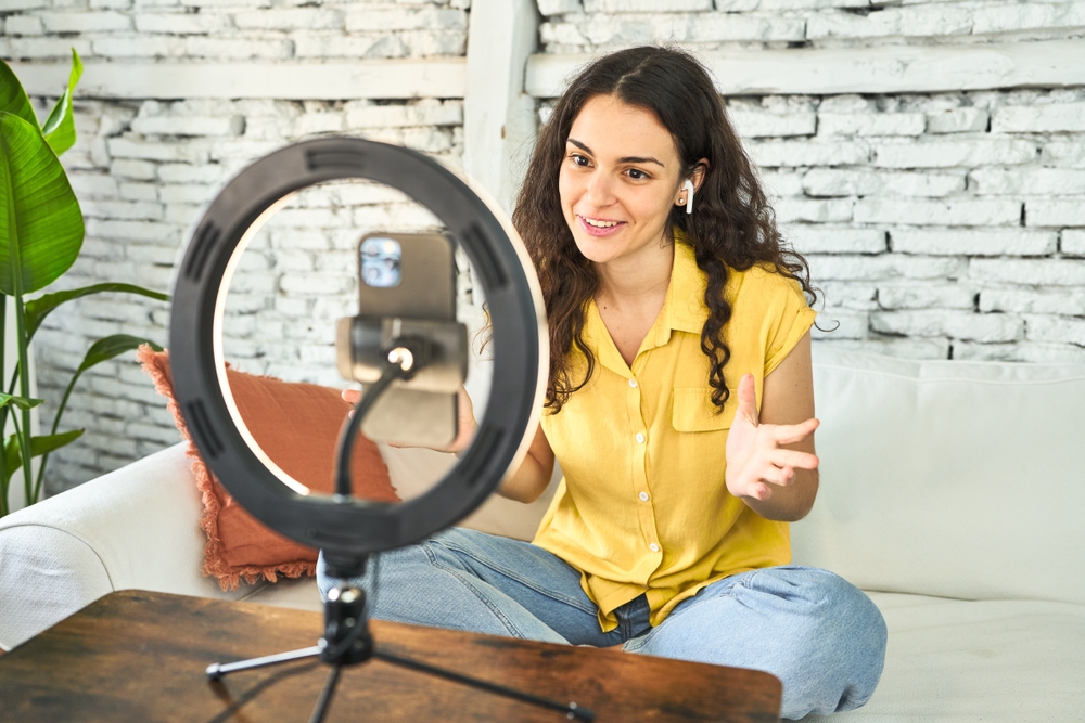 An insurance agent creatively recording a vlog on her sofa with a ring light and mobile, sharing inspiration and connecting online to generate leads and gain clients.