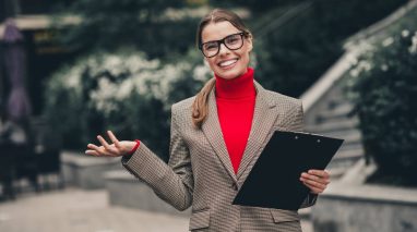 An insurance agent in fall-inspired attire holding a clipboard, presenting a confident and cheerful expression against an urban outdoor background, ready to use fall strategies for insurance agents.