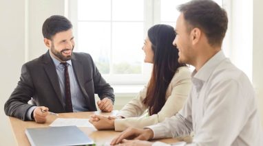 Independent agent sitting at a table, smiling while speaking with a couple who want to resolve their insurance lead questions before getting a policy.