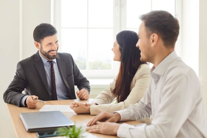Independent agent sitting at a table, smiling while speaking with a couple who want to resolve their insurance lead questions before getting a policy.