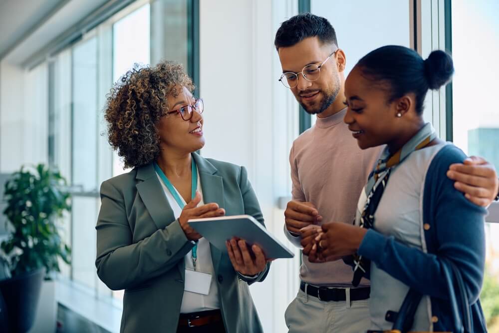 Independent insurance agent holding a tablet while speaking with an embracing couple, answering their insurance lead questions.