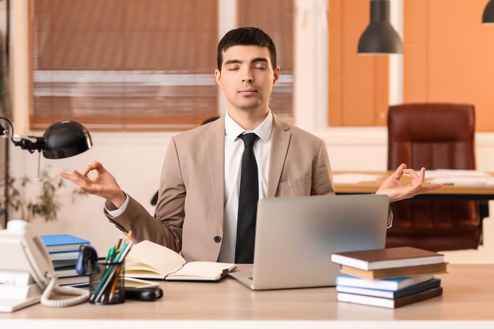 A man in an office meditating in front of his desk, relaxing after learning techniques for independent insurance agents work-life balance.