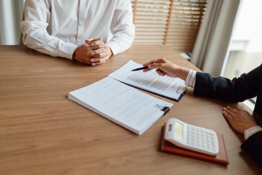 Insurance agent explaining policy documents to a client across a desk with paperwork and a calculator during an insurance consultation.